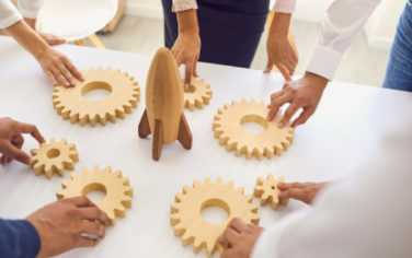 A group of hands touch wooden gears around a wooden rocket